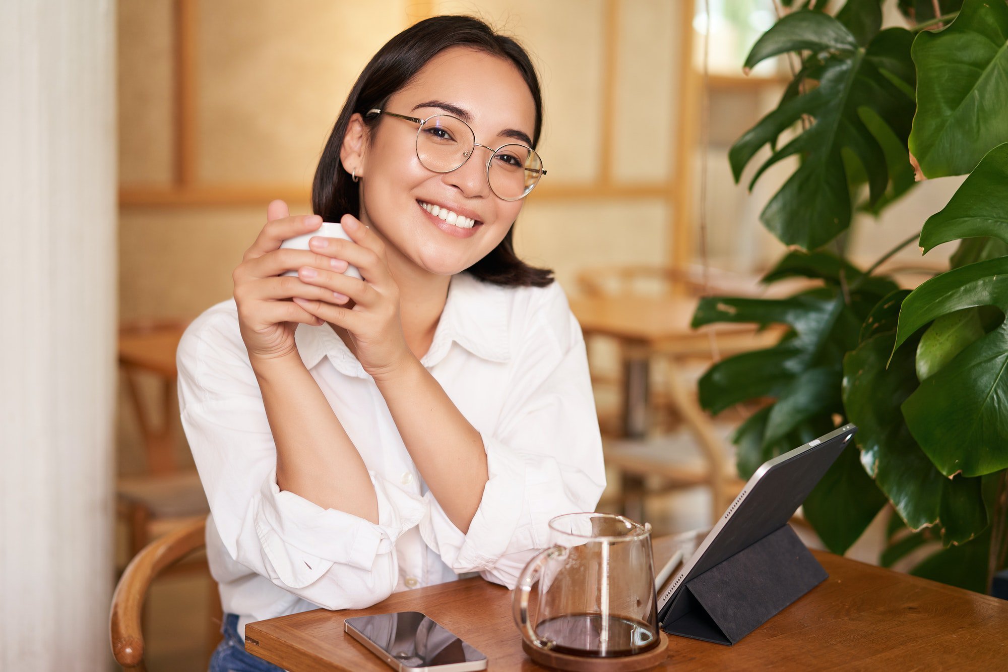 Smiling asian girl in glasses, woman working on remote, drinking coffee and using tablet